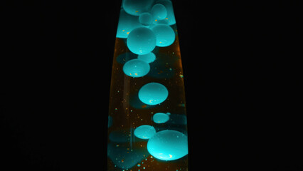 Close up view of lava lamp with blue moving bubbles. Concept. Beautiful glass lava lamp with liquid substance inside standing isolated on black background.