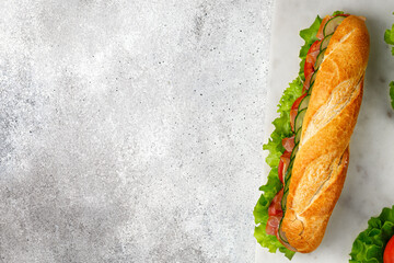 Baguette with ham and vegetables. Sandwich with ham, tomato, lettuce salad, cucumber on marble...