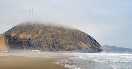 Mountain within fog and sandy coastline of pacific ocean