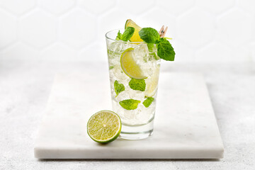 Mojito, Iced cold summer drink. Glass of cold tonic with lime. Lemonade with ice and mint on marble board and grey background. Copy space