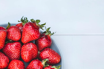 Delicious, fresh strawberries in a stylish plate on a white wooden background. Top view with space to copy.