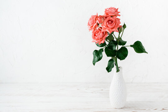 A branch of a spray pink rose in a decorated vase on a light background. Lifestyle and copy space
