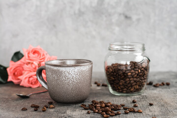 Latte in a ceramic cup, jar with coffee beans and roses on the table.