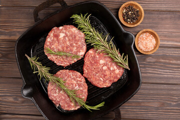 Homemade minced pork and beef patties, with spices, rosemary, ready for roasting, for cooking burgers on a cast-iron grill pan, on a wooden background, flat lay, open space
