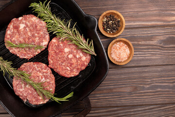 Homemade minced pork and beef patties, with spices, rosemary, ready for roasting, for cooking burgers on a cast-iron grill pan, on a wooden background, flat lay, open space