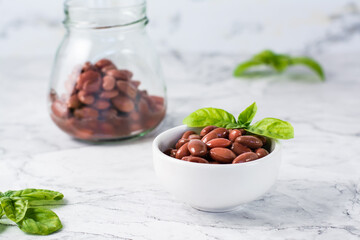 Boiled red beans in a bowl and jar and basil leaves on the table. Meat protein alternative