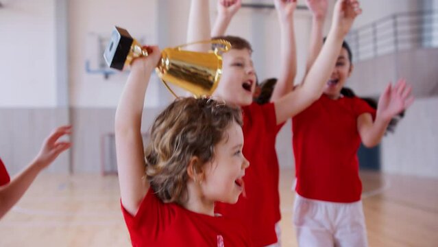 School sports teammates rising up golden trophy after winning sports indoor competition