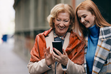 A grandmother and her grandchild standing on the street and reading messages on the phone.