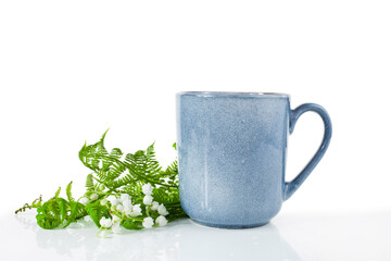 Blue ceramic cup with lily of the valley or may bells flowers and fern leaves isolated on a white...