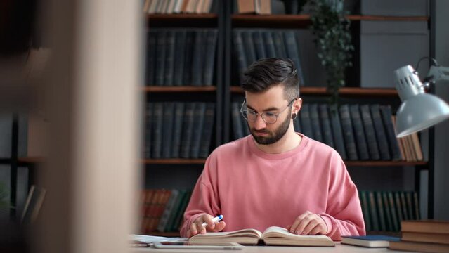 Confident male student studying paper book making notes prepare exam at college public library desk