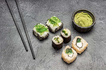 Sushi set with seaweed, black sesame and cucumber. Chopsticks, wasabi in black bowl.