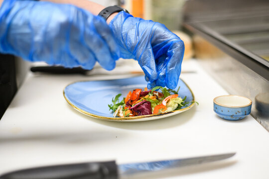 Close-Up of a person wearing disposable protective gloves putting salad on a plate in a cafe