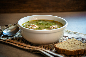 Homemade appetizing, delicious soup with meatballs, homemade bread, kitchen national napkin, and spoon on the kitchen dining table.