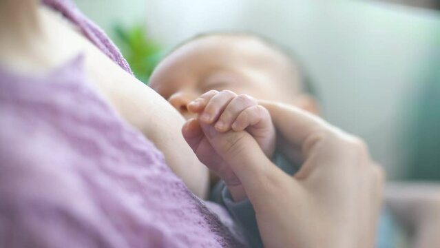A young mother breastfeeds a newborn baby in a light bedroom. Mom holding her Baby and hugging. Maternity, Parenthood and Motherhood. Beautiful Happy Family. Close-up, tilt shift lens