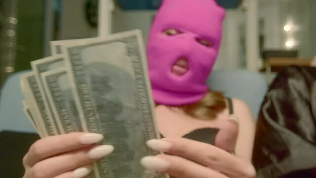  A girl in a pink mask who counts money. Footage. A young girl in a rubber mask and underwear, sitting on a leather sofa and counting large sums.