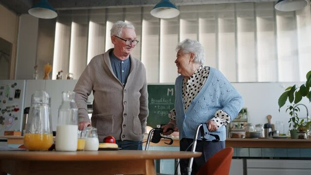Senior man and woman walking with walker indoors in retirement nursing hme.