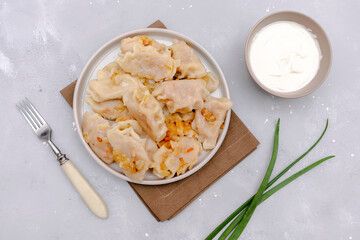 Homemade dumplings, vareniki, varenyky, pyrohy with stewed cabbage fried with onion on plate.Traditional ukrainian popular national dish,cuisine served with sour cream on gray background