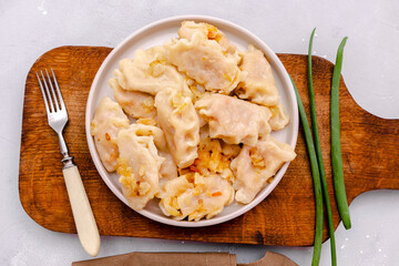 Homemade dumplings, vareniki, varenyky, pyrohy with stewed cabbage fried with onion on plate.Traditional ukrainian popular national dish,cuisine served with sour cream on wooden board, gray backgound