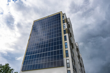 Fototapeta premium solar panels on the wall of a multi-storey building on storm clouds background. Renewable solar energy. an energy-efficient home that uses the energy of the earth, sun, air and wastewater