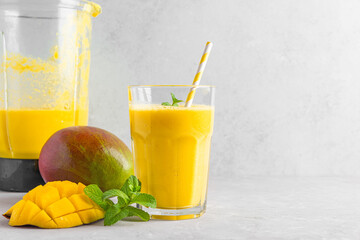 Glass of yellow mango smoothie with fresh juicy fruits and blender for making healthy summer drink