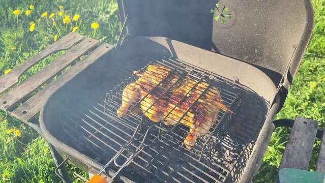 Cooking grilled chicken food outdoors. The hand opens the lid of the barbecue
