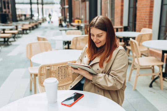 Young woman enjoying a coffee, sitting on the cafe terrace on the modern city street. Person sitting at table and using tablet outdoors. Traveler, Online education, working or shopping concept