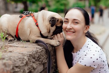 Young girl goes for walk with doggy pug in park. Selective focus.