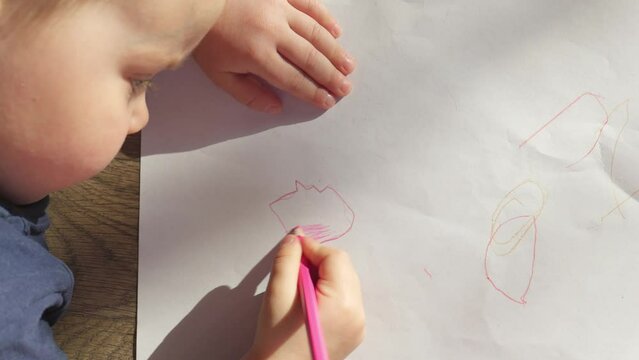 baby drawing on the floor at home using color pencils, leisure activity at home. back to school concept, child boy coloring flower, heart shape red figure. kid developing imagination, art learning