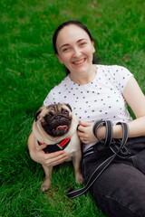 Young girl goes for walk with doggy pug in park. Selective focus.