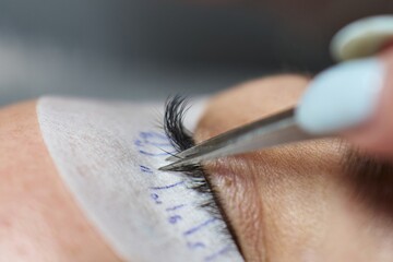 close-up of thin tweezers holding the cilia highlighting one to stick a bunch of lash extensions to...