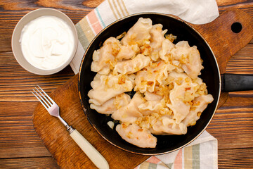 Homemade dumplings, vareniki, varenyky, pyrohy with stewed cabbage fried with onion on pan.Traditional ukrainian popular national dish,cuisine served with sour cream on wooden board