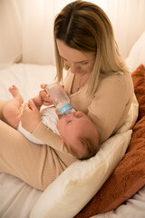 mom feeds a newborn baby with a bottle. the sun is shining in the background.