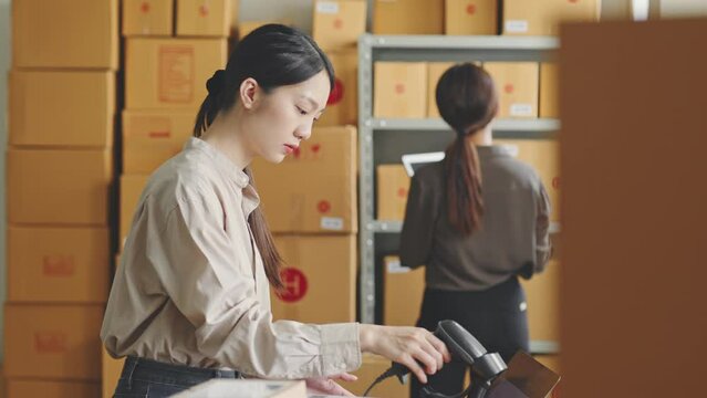 Asian woman working at online store warehouse, using barcode reader check on customer parcel box, online e-commerce retail small business concept