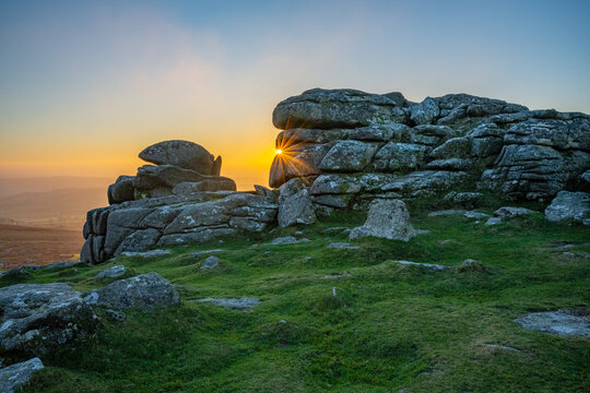 Sunburst through a granite tor, Dartmoor National Park, Devon, England, UK