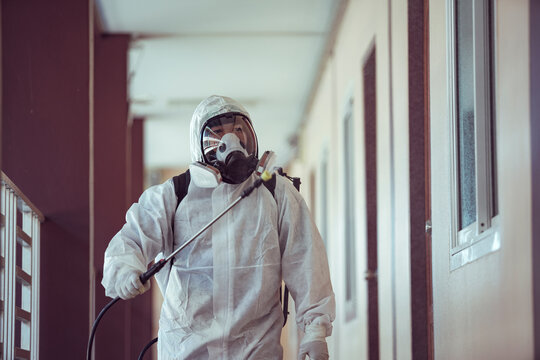 Cleaner in PPE spraying disinfectant inside a building