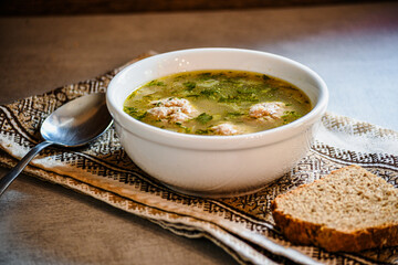 Homemade appetizing, delicious soup with meatballs, homemade bread, kitchen national napkin, and spoon on the kitchen dining table.