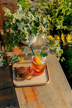 Fresh homemade peach ice tea with mint, chocolate chip cookie served on table outdoors. summer cold fruit drink in sunny afternoon with yellow flowers behind