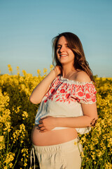 Naklejka na ściany i meble A pregnant woman in a Ukrainian embroidered shirt stands in a rapeseed field