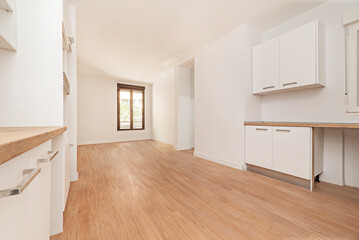 Photo of a kitchen open to a living room with white wood cabinets with wood countertops and matching hardwood floors.