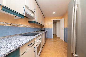 Picture of a kitchen with glossy wood cabinets, a large gray fridge, and a countertop with blue...