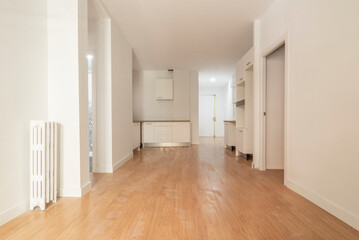 Empty living room with kitchen cabinets on one wall, freshly painted walls, light oak flooring and vintage cast iron radiators
