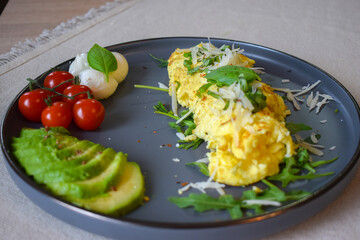 French omelette dish. Delicous homemade french omlette filled with cheese. Plating with fresh vegetables like avocado, cherry tomatoes, but also basil and mozzarella.