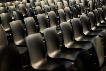 Black plastic chairs stand in rows. Black chairs with backs 