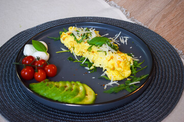 French omelette dish. Delicous homemade french omlette filled with cheese. Plating with fresh vegetables like avocado, cherry tomatoes, but also basil and mozzarella.