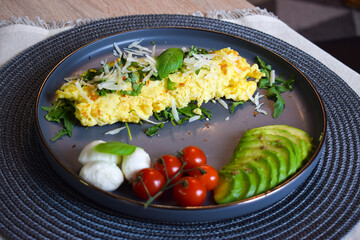 French omelette dish. Delicous homemade french omlette filled with cheese. Plating with fresh vegetables like avocado, cherry tomatoes, but also basil and mozzarella.