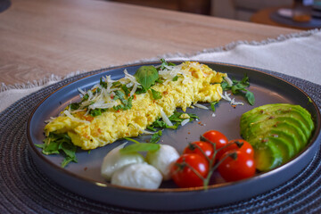 French omelette dish. Delicous homemade french omlette filled with cheese. Plating with fresh vegetables like avocado, cherry tomatoes, but also basil and mozzarella.