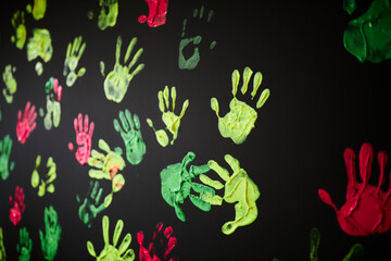 multi-colored handprints on a black background. Handprints in acrylic paint.