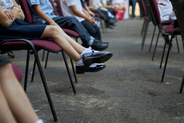 Obraz premium schoolchildren sit on chairs in the backyard of the school, close-up of legs