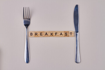 Cutlery and word breakfast made from vintage wooden cubes on white background. Flat lay.