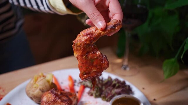 closeup of hand dipping roasted chicken tabaka in tomato sauce on white plate